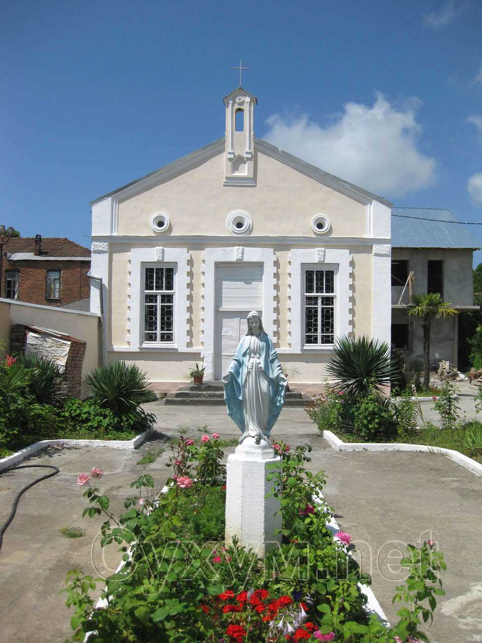 цветы и статуя девы марии перед католическим храмом